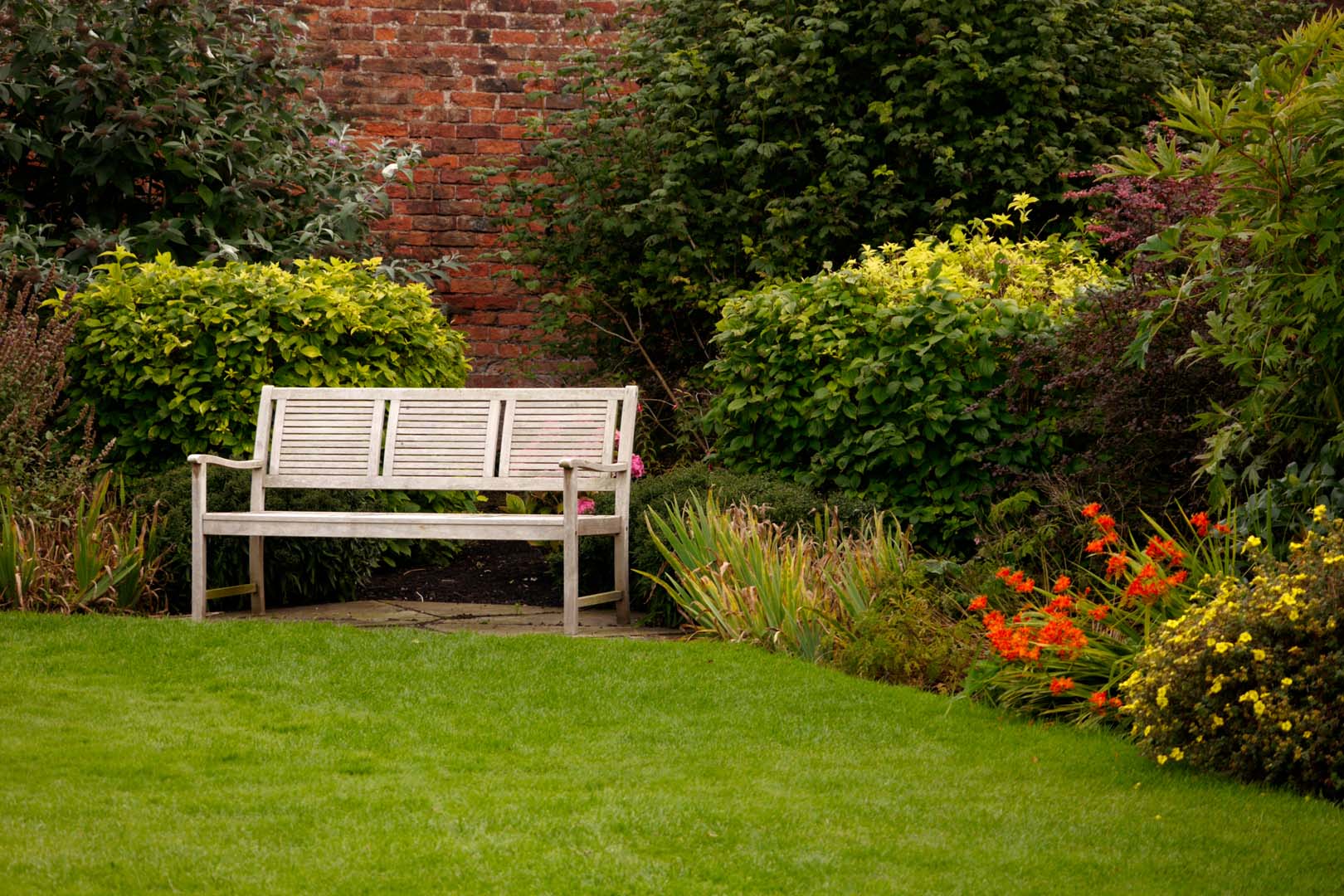 Garden maintenance in Mackworth with a neat lawn, tidy borders and a seating area in front of a brick wall